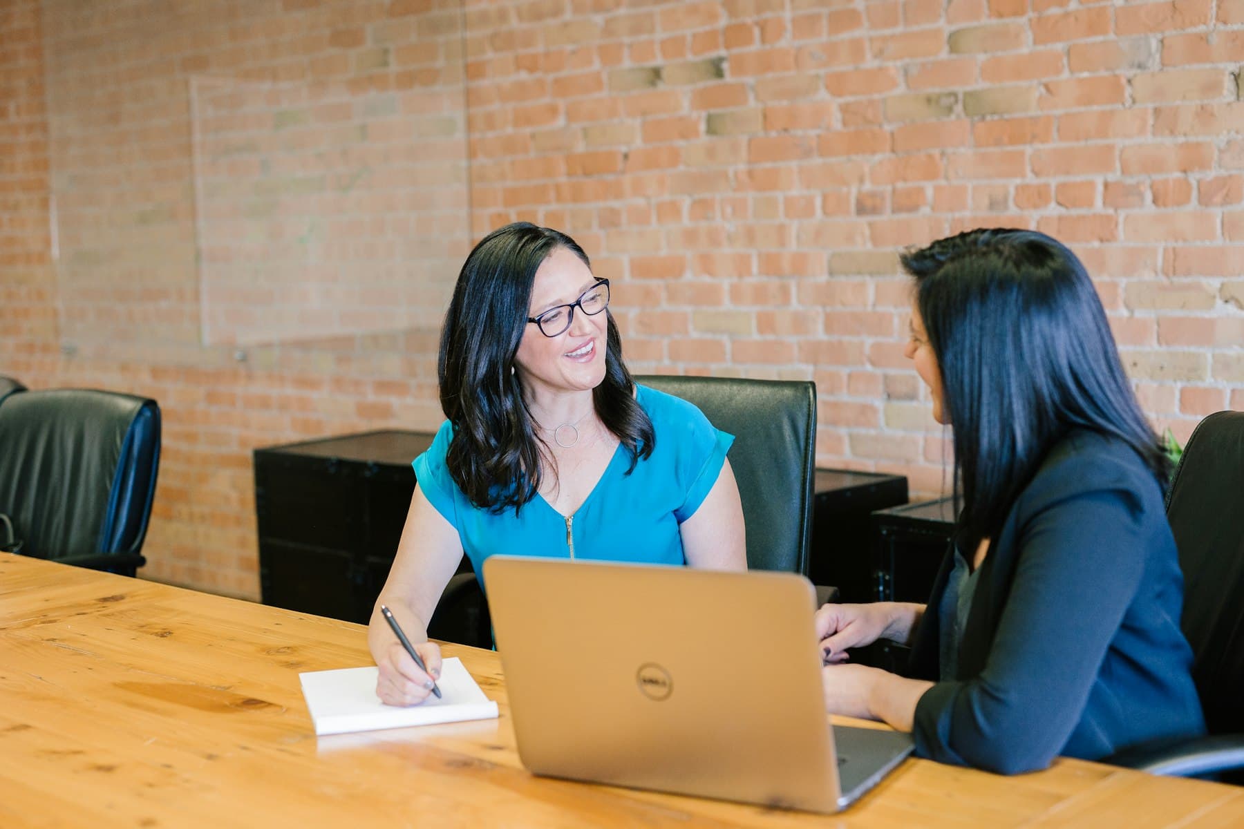 Two people talking across a table with a laptop and notebook