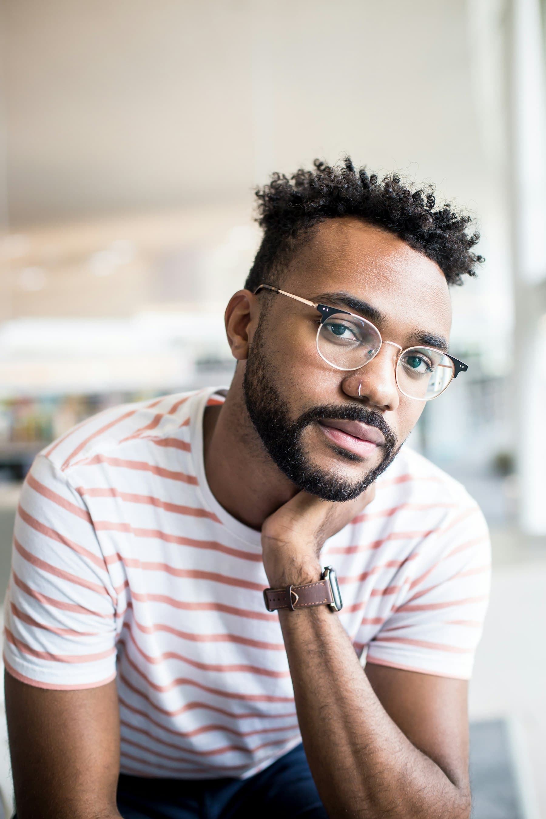 Man in glasses and a striped T-shirt, resting his chin on his hand