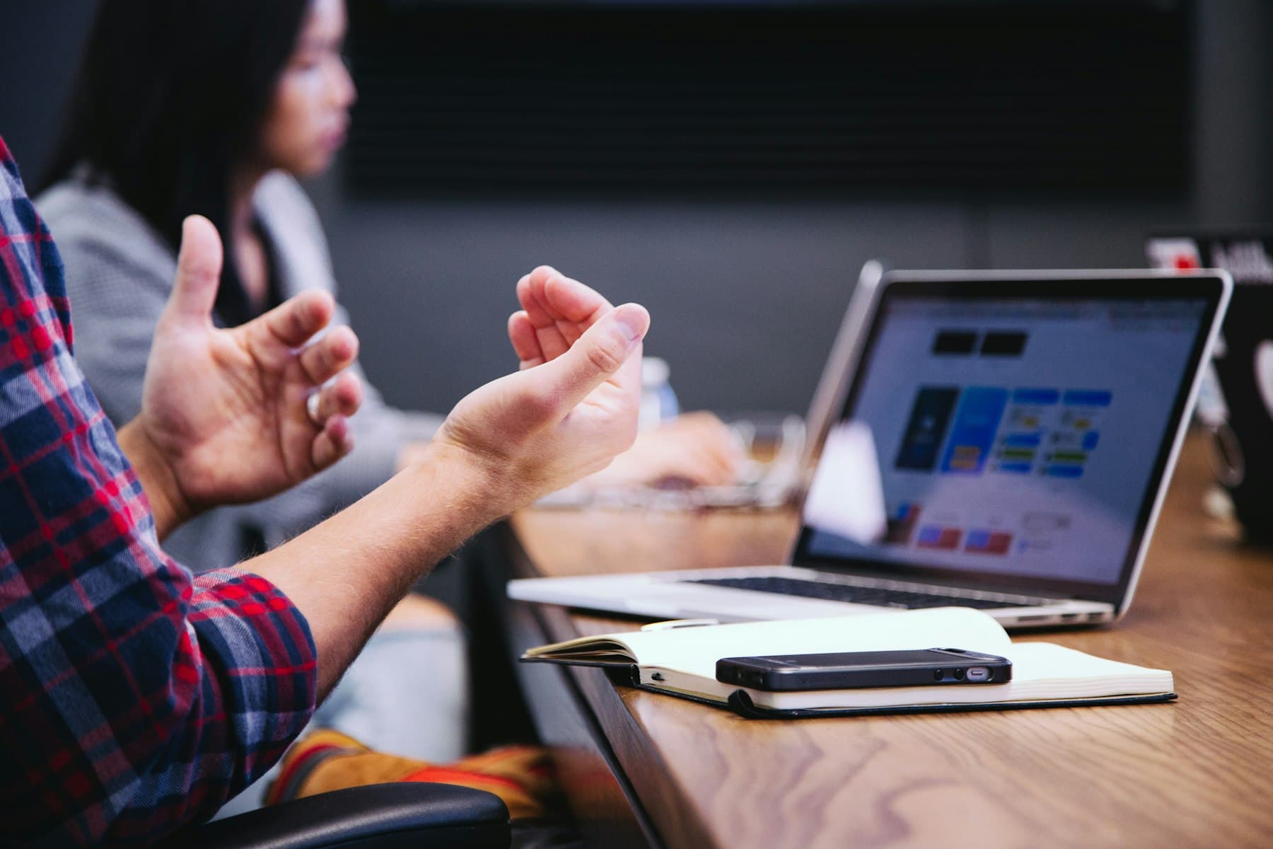 Hands gesturing over a laptop and notebook during a meeting