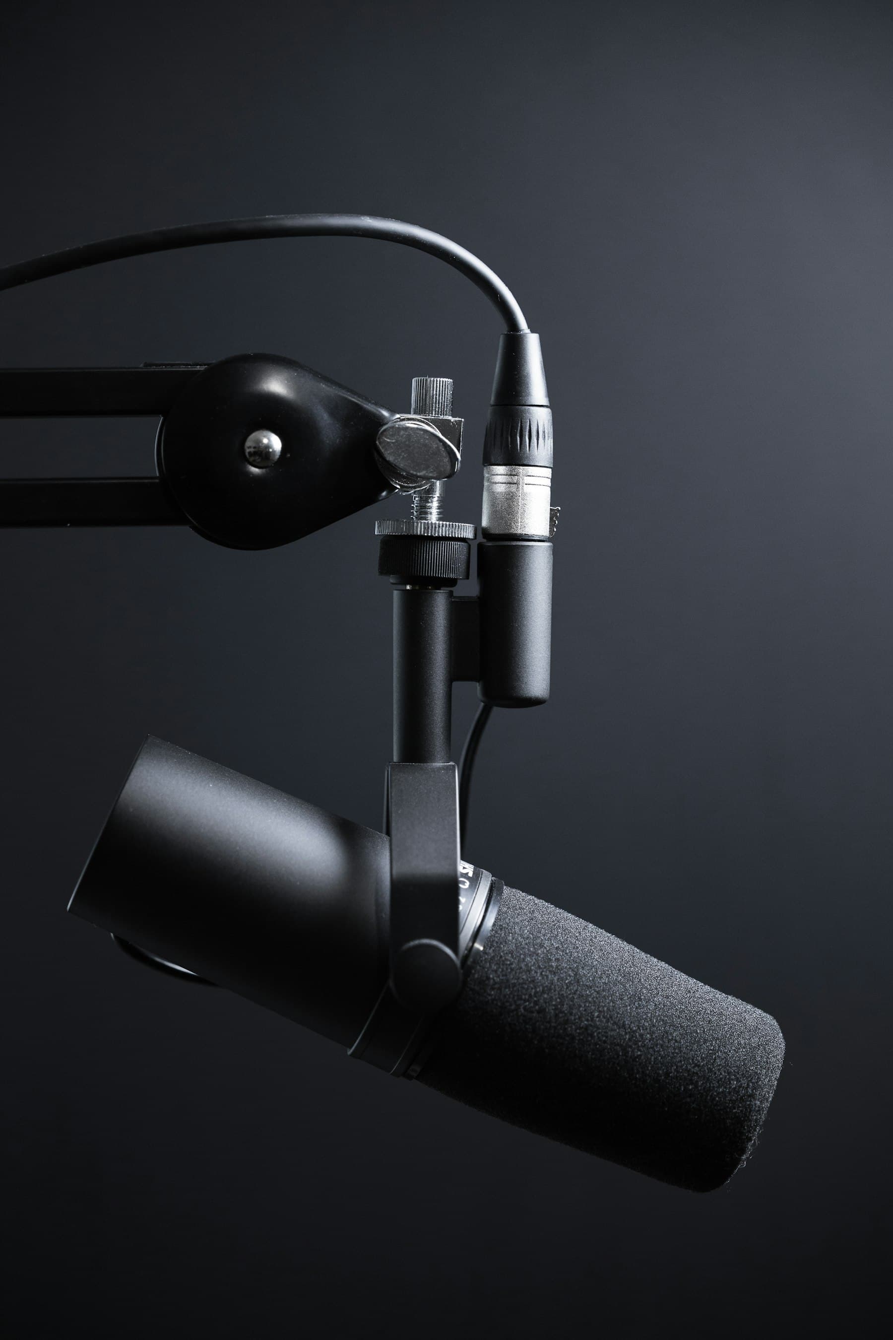 A broadcast microphone on a boom arm against a dark wall
